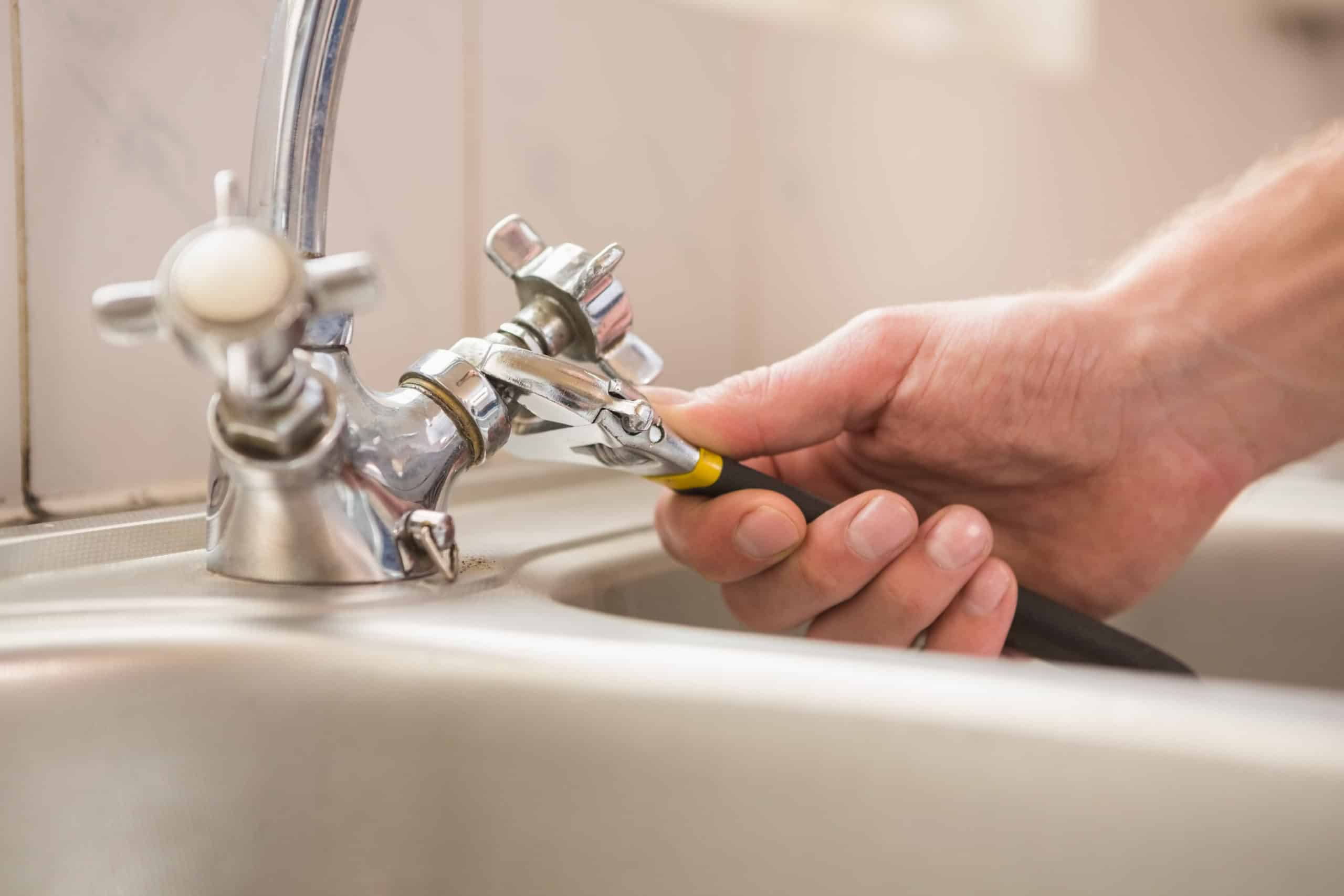 Man fixing tap with pliers at home in the kitchen